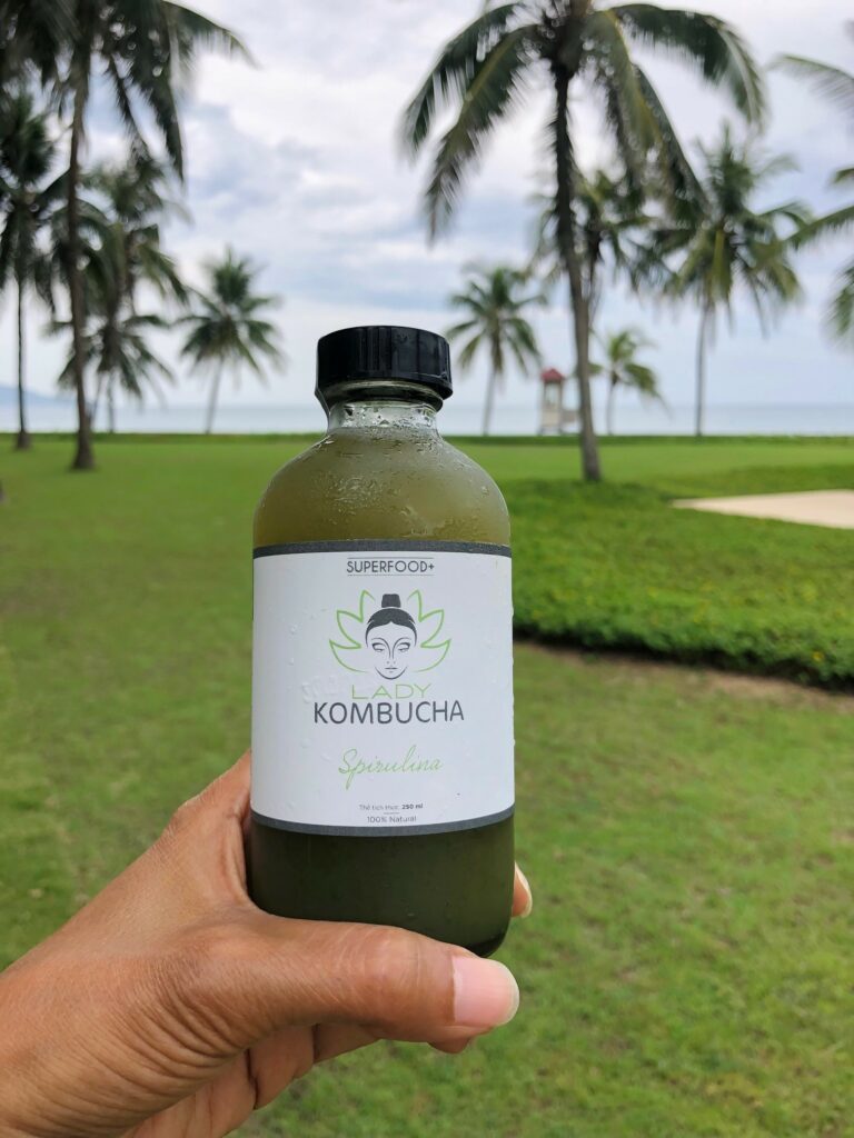 Bottle of spirulina Kombucha from Lady Kombucha in Danang in front of the sea with palm tree